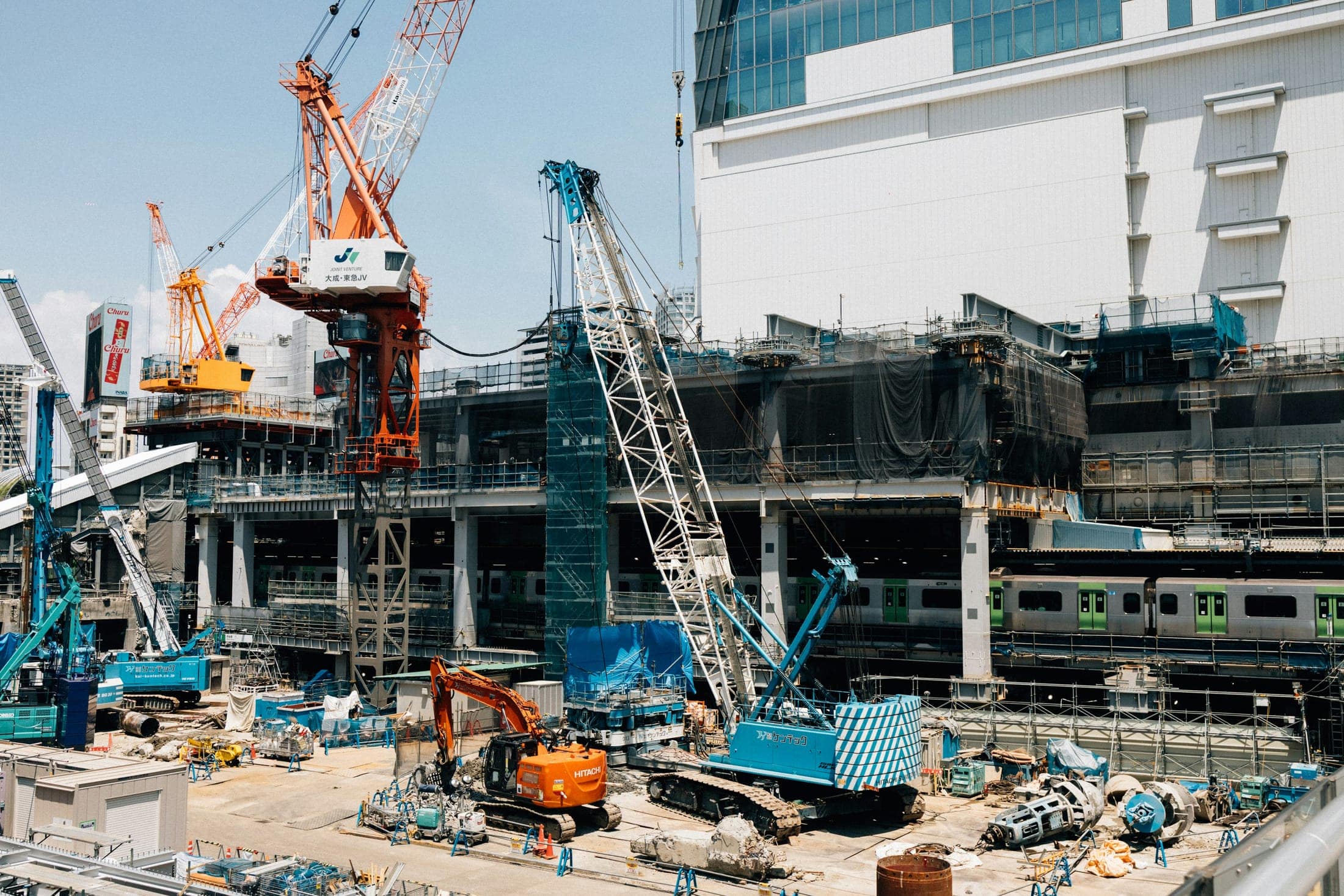 Tower cranes and crawler cranes at a major infrastructure construction site above an active rail line