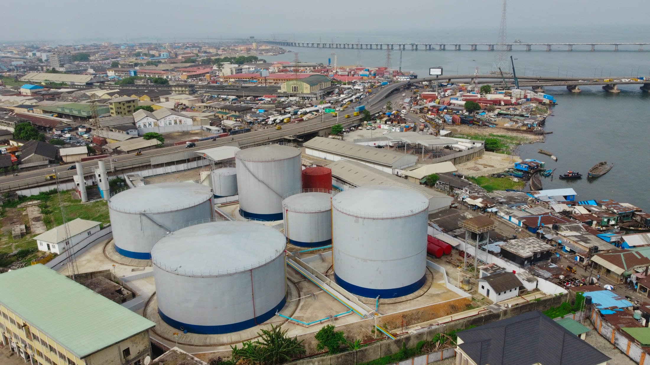 Aerial view of a petroleum storage terminal with large storage tanks beside a coastal port and river crossing